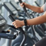 A person using a fitness tracker while exercising on an elliptical machine in a gym.