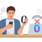 A person holding a fitness tracker and an iPhone with a confused expression, sitting at a desk with a laptop showing a Bluetooth connection failure.