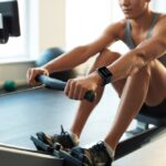A person rowing on a rowing machine while wearing a smartwatch that displays workout data.