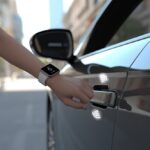 A person using a smartwatch to unlock a car by holding their wrist close to the car door handle.