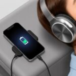 A person wearing Bluetooth headphones while charging their smartphone indoors.