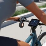 How to Use Bluetooth Headphones with a Smart Bike Without Turned Heads or Tangled Wires Person riding a smart bike wearing Bluetooth headphones with a digital display on the bike's handlebar.