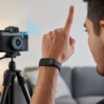 How to Use a Fitness Tracker as a Camera Remote: Snap Pics While Counting Steps A person using a fitness tracker on their wrist to remotely control a camera on a tripod.