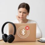 Why do my Bluetooth headphones not pair with my laptop? Gremlins, Gobbled Signals, and Other Tech Mysteries A person at a desk looking frustrated while trying to connect Bluetooth headphones to a laptop that shows a failed connection symbol.
