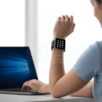 How to Use a Smartwatch with Windows PC and Feel Like a Secret Agent A person wearing a smartwatch is using a Windows laptop, with a visual connection indicating syncing between the devices.