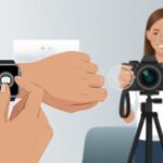 A person pressing a button on their smartwatch to remotely control a camera on a tripod, with another person posing in the background.