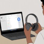 A person sitting at a desk using a Chromebook laptop with Bluetooth headphones nearby, showing the process of connecting the headphones to the laptop.