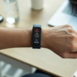 Close-up of a person’s wrist wearing a fitness tracker showing health data with a subtle alert icon, set against a clean workspace background.