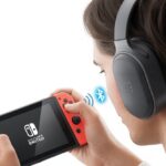 How to use Bluetooth headphones with Nintendo Switch and Finally Enjoy Wireless Freedom A person wearing Bluetooth headphones while holding a Nintendo Switch in handheld mode, showing a wireless connection between the headphones and the console.