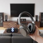 A person holding Bluetooth headphones wirelessly connected to a home theater system with a TV and speakers in a living room.