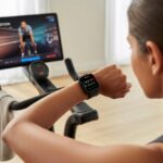 How to use a smartwatch with Peloton Without Accidentally Calling Your Mom A person riding a Peloton bike indoors while checking their smartwatch displaying fitness data.