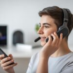 A person wearing Bluetooth headphones and holding a smartphone, engaged in a phone call in a home setting.
