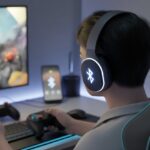 A person wearing Bluetooth headphones playing a video game on a computer with gaming accessories around them.