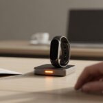 Why is my fitness tracker not responding after charging? Tech Troubles That Need More Than a Power Nap A close-up of a fitness tracker on a table next to its charger, with a hand reaching toward it and an open manual nearby.