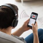 How to use Bluetooth headphones for YouTube Without Accidentally Broadcasting to the Whole Room A person wearing Bluetooth headphones and holding a smartphone showing a video playing, with wireless connection symbols around them.