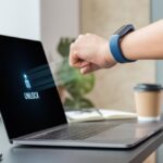 How to use a fitness tracker for unlocking your computer: Because Passwords Are So 2024 A person wearing a fitness tracker on their wrist is unlocking a laptop on a desk in a modern workspace.